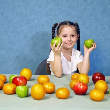 portrait of a cute little girl with fruits indoors. ripe fruit on the table. beautiful smiling child playing with fresh apples on the table.