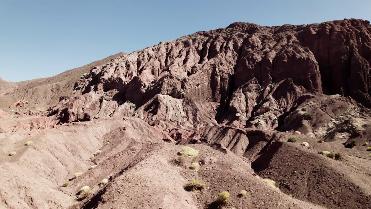 Aerial view of eroded red rock formations in the Atacama Desert, Chile. Harsh sunlight reveals layers of volcanic sediment and sculpted cliffs