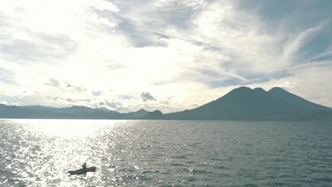 drone aerial flying over lake atitlan, guatemala surrounded by beautiful volcanoes and rotating around a man kayaking