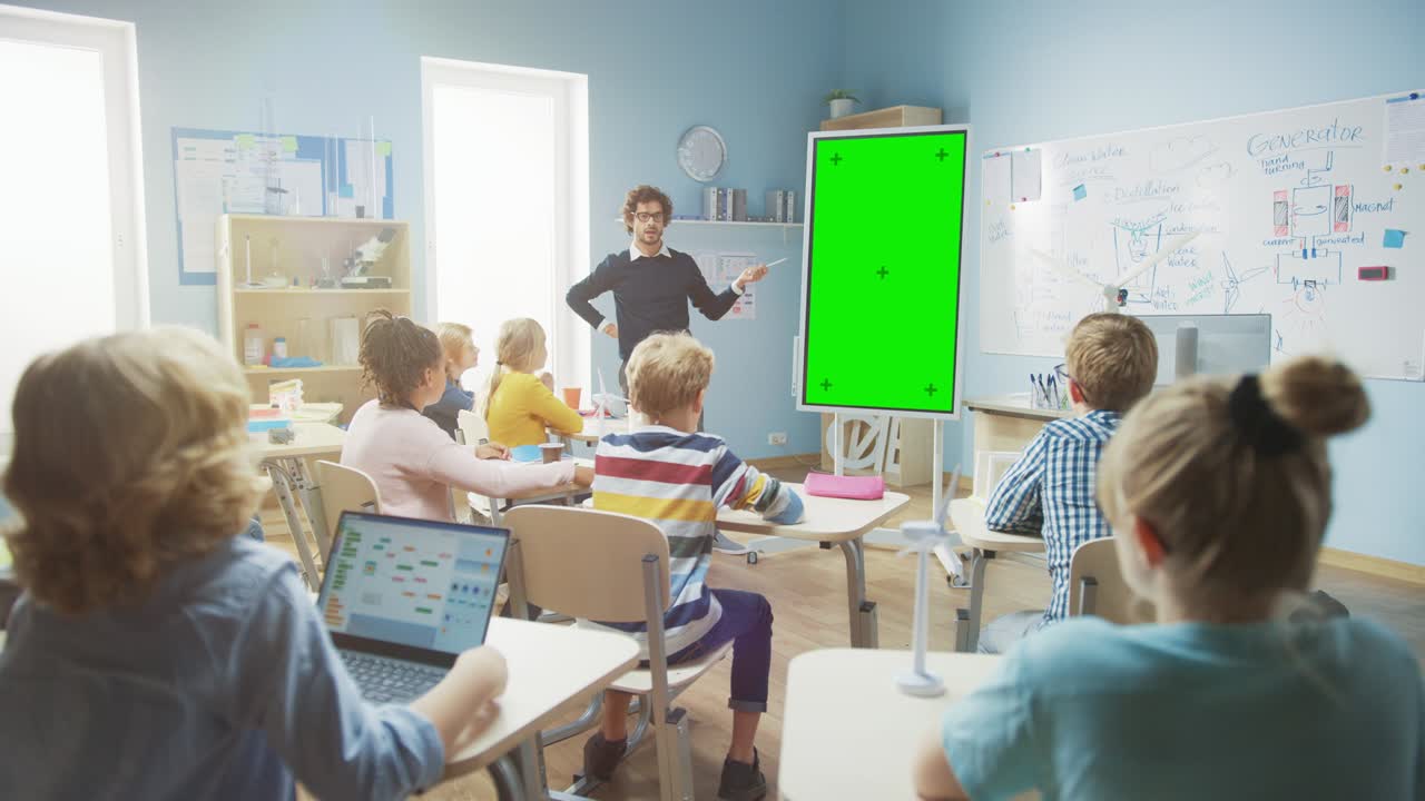 In the Elementary School Classroom: Teacher Uses Vertical Green Mock-up Screen Interactive Digital Whiteboard to Explain Lesson to Diverse Group of Schoolchildren. Multi Ethnic Kids Learning Science