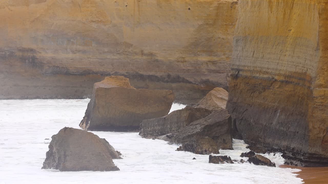Dynamic ocean waves crash against rugged cliffs at Port Campbell, Australia. Overcast lighting enhances the dramatic coastal landscape