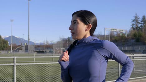 Determined-young-woman-jogging-on-track-and-field-path,-Closeup-Follow-Shot