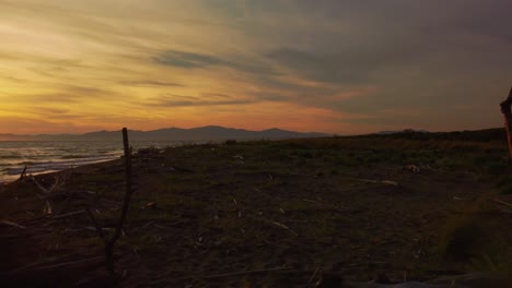 Slow-cinematic-close-up-aerial-drone-footage-of-the-sunset-at-a-sandy-beach-at-the-seaside-near-Alberese-in-the-iconic-Maremma-nature-park-in-Tuscany,-Italy,-with-waves,-islands-and-a-dramatic-red-sky