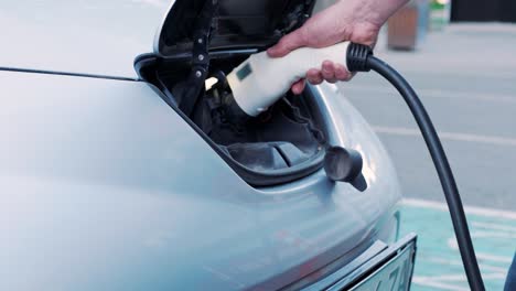 proceso de reabastecimiento de combustible de un automóvil eléctrico. un disparo debajo de la escotilla donde se carga el automóvil ecológico eléctrico. la escotella de carga del automóvil eléctrico se abre automáticamente. una mano masculina inserta un automóvil erecto