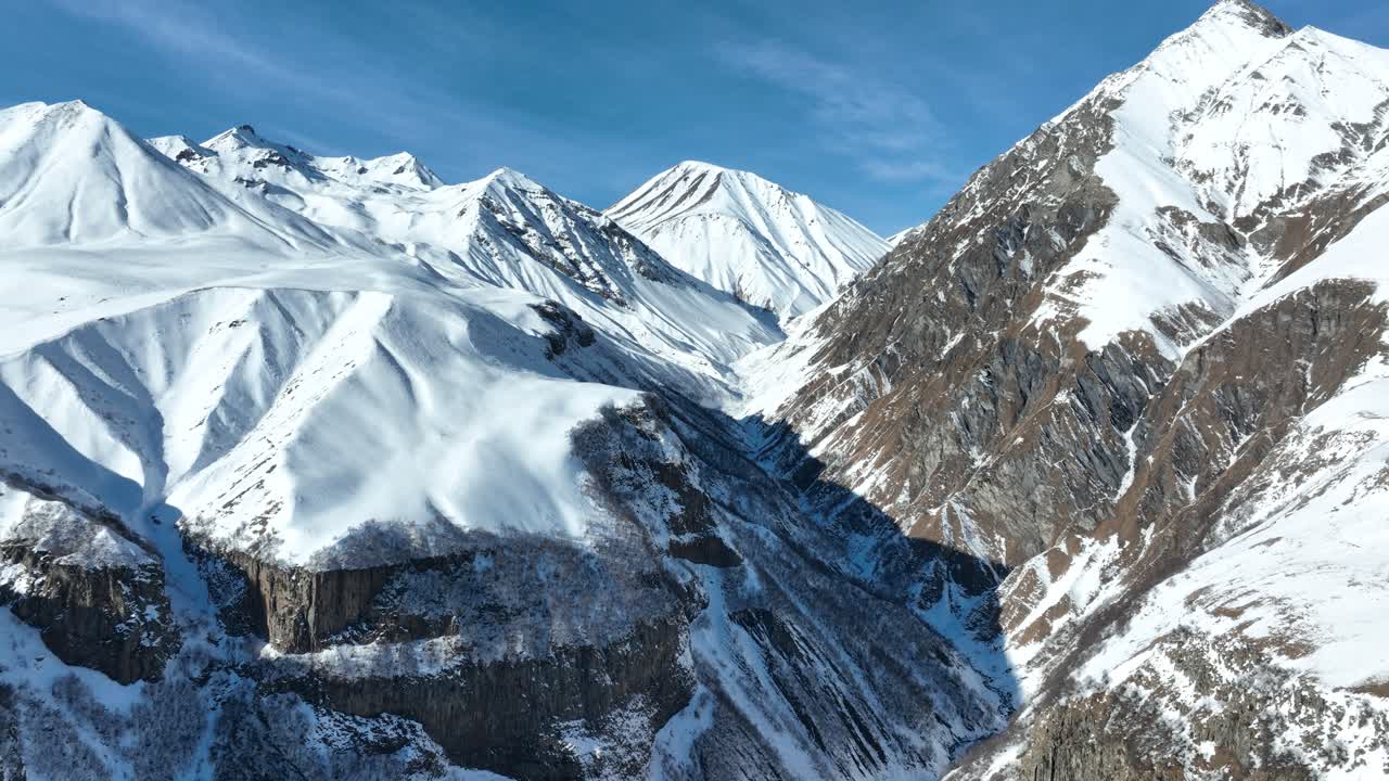 Towering snow-capped peaks bask in the soft winter sunlight, creating a striking panorama of alpine beauty. The rugged cliffs and valleys epitomize untouched wilderness