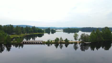 Drone-shot-of-a-lake-and-sandy-road-with-a-bridge-causeway-in-the-Adirondack-mountains-on-a-calm-day