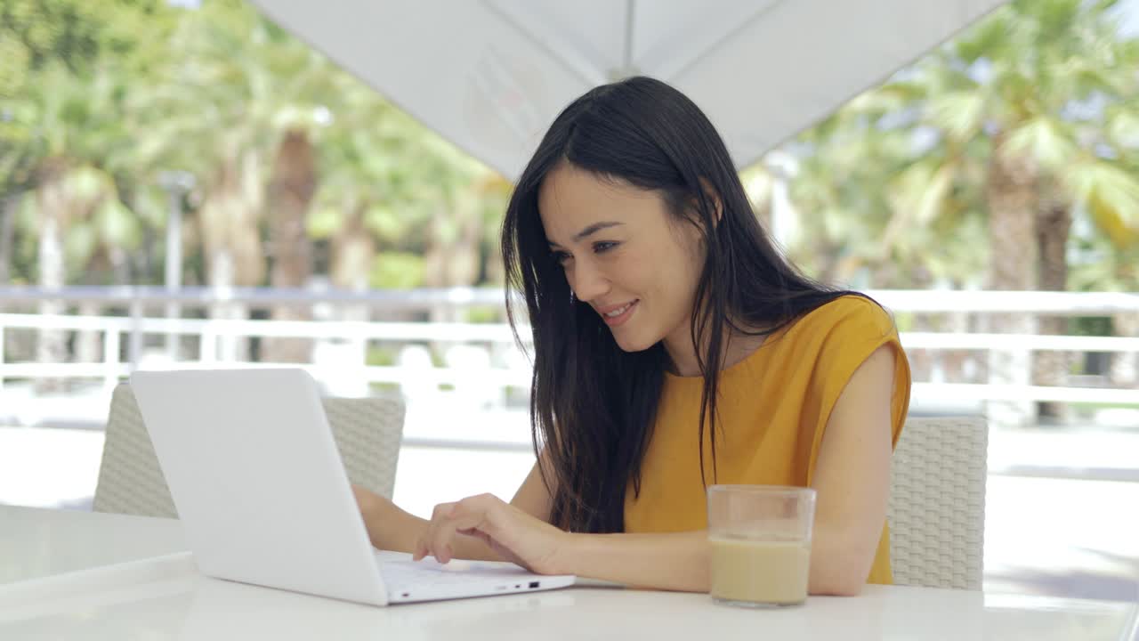 joven empresaria con aparatos y café en vaso sentado en la cafetería al aire libre
