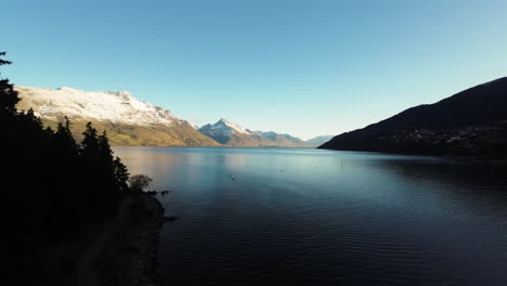 aerial cinematic shot of snow-capped mountains overlooking a lake in queenstown