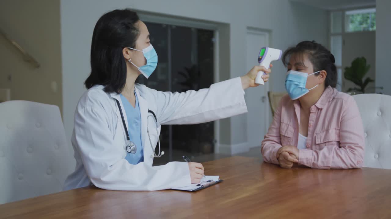 アジア系の女性看護師がマスクを着用し、病院でマスクを着用した女性患者の体温を測っている。
