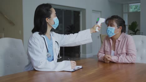 asian female nurse wearing face mask taking temperature of female patient wearing mask in hospital