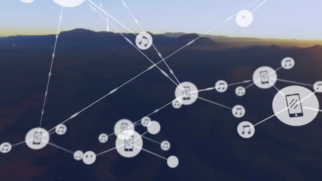 animation of network of digital icons against aerial view of mountains against sunset sky