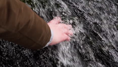 nahaufnahme einer weiblichen hand, die in zeitlupe eiskaltes wasser aus dem wasserfall berührt