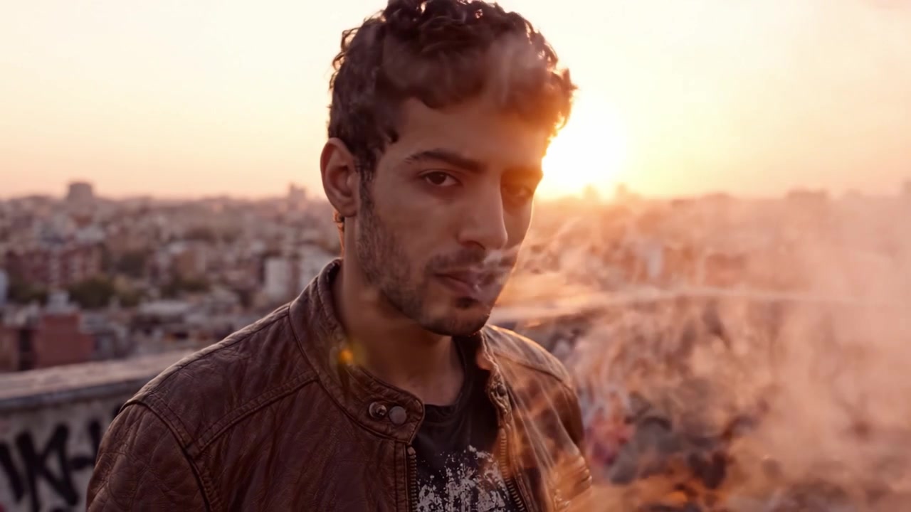 Un momento contemplativo al atardecer, mostrando a un individuo reflexionando sobre la vida mientras disfruta de un cigarrillo en la azotea llena de grafitis con vistas a una extensa ciudad.