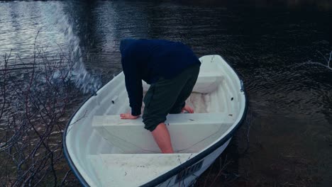 a man bails water from a small boat using a plastic container near the shore in reinsjøen, åfjord, trøndelag, norway - close up