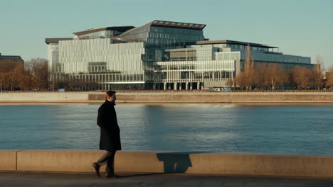 man walking along a riverfront in a modern city
