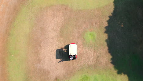 aerial drone shot of gold cart driving on fairway of golf course