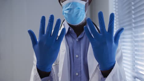 midsection of mixed race male doctor wearing face mask and surgical gloves