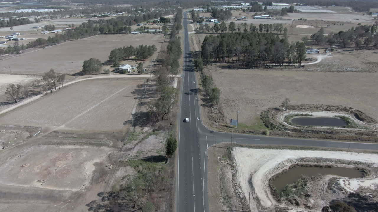 plano general aéreo que se acerca a un vehículo blanco que circula por una carretera junto a las granjas, en stanthorpe, queensland, australia
