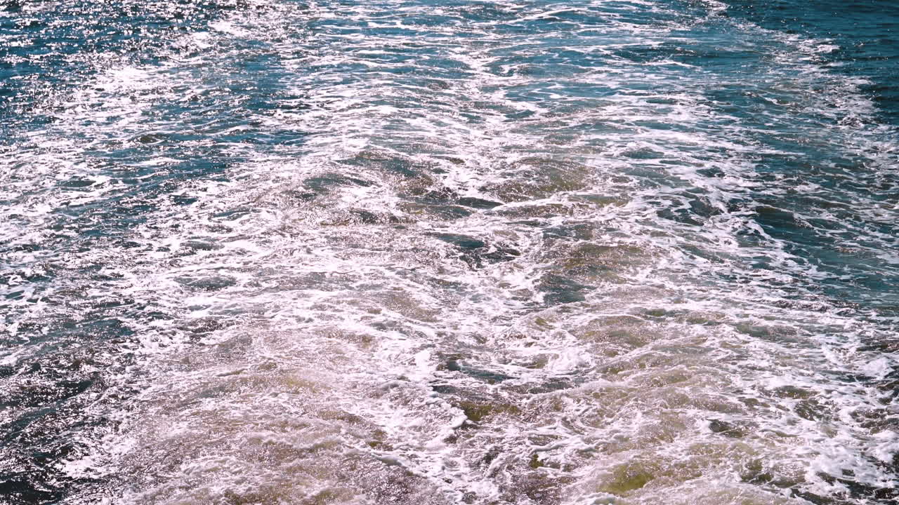 Turbulente, wervelende textuur van een wateroppervlak met kielzog en reflecterend zonlicht. Een close-up van het kolkende, schuimende water achter een bewegend vaartuig op een heldere, zonnige dag