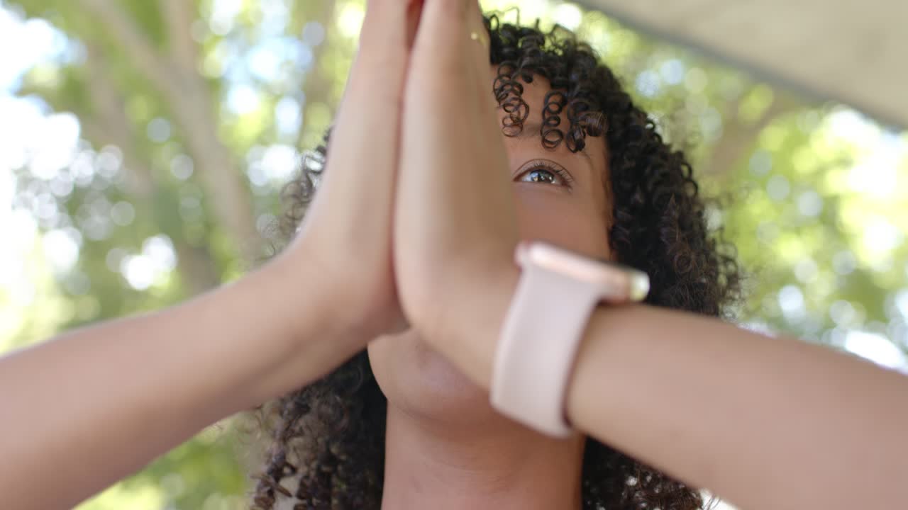 African American woman in sun raising arms, breathing and centering under trees with watch and ring