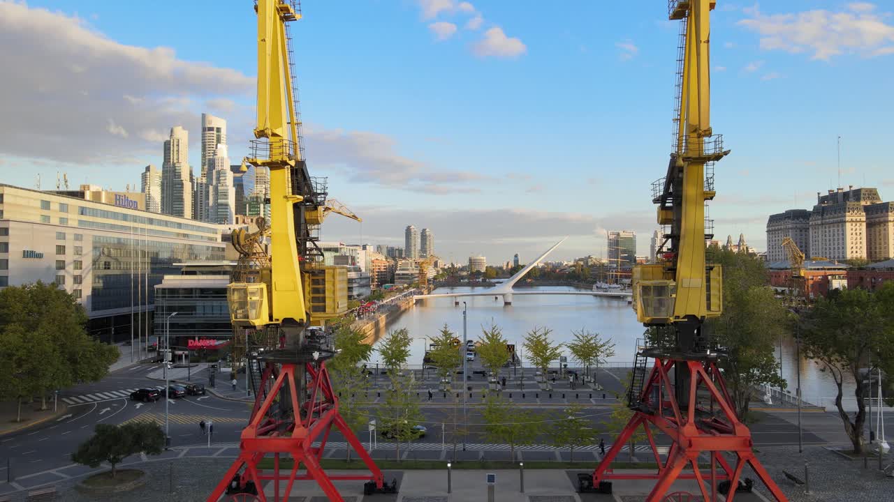 dolly aéreo hacia adelante volando entre dos antiguas grúas portuarias y revelando el barrio turístico de puerto madero.