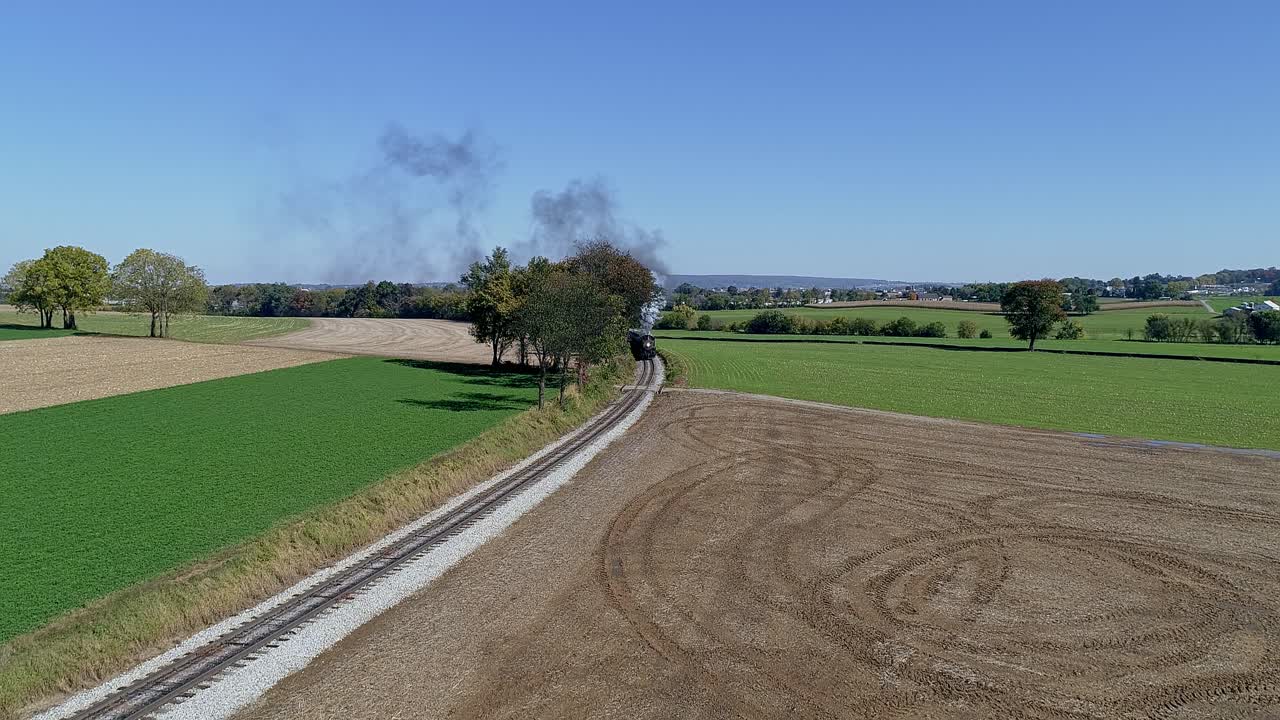 vista de drones de un tren de pasajeros de vapor que redondea una curva que sopla humo y vapor en un día soleado de otoño