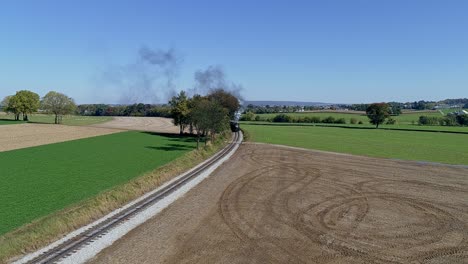 drone view of a steam passenger train rounding a curve blowing smoke and steam on a sunny fall day