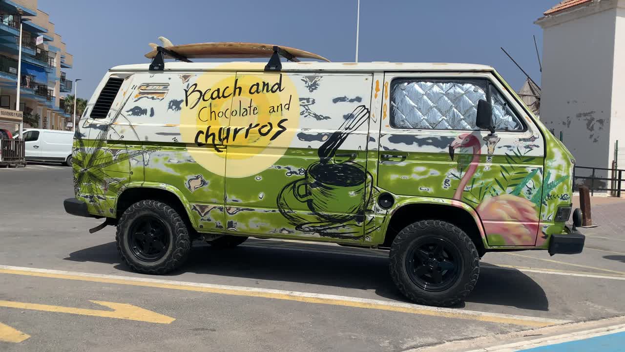 A vibrant, multicolored old Churros vehicle is parked in front of a residential building, adding a nostalgic and lively touch to the urban scene