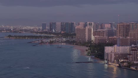 Toma-Panorámica-Aérea-De-Modernos-Complejos-Turísticos-Iluminados-En-Waikiki-Al-Atardecer