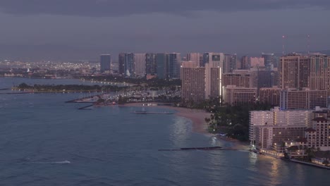 aerial panning shot of modern illuminated high resorts at waikiki at dusk