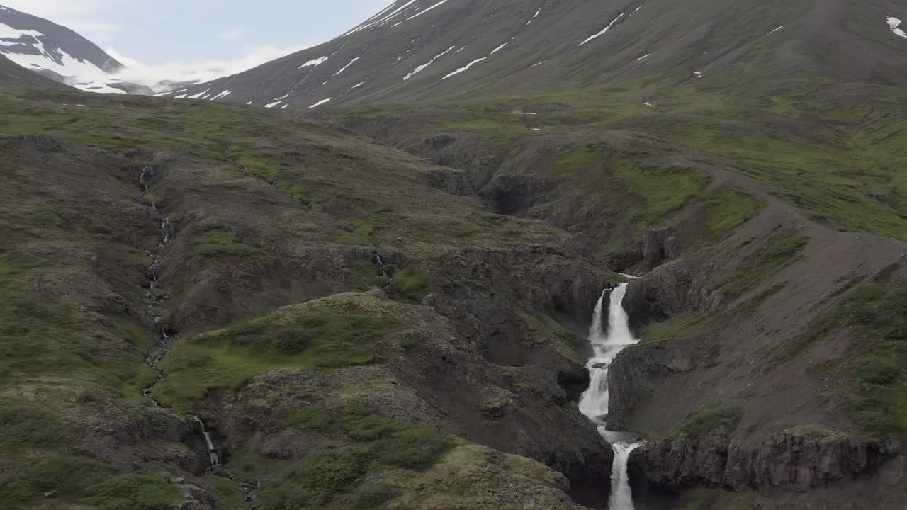 cascada rodeada de grandes montañas majestuosas en el valle de fagridalur de islandia