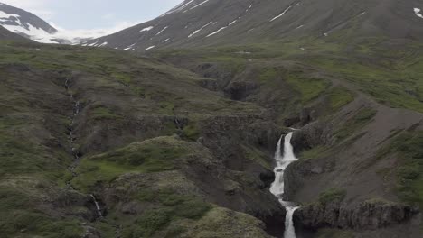 Waterfall-surrounded-by-large-majestic-mountains-in-Fagridalur-valley-of-Iceland