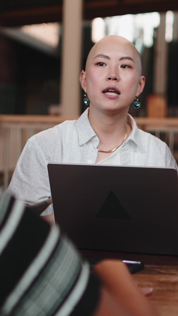 Bald Asian Woman Discussing Work with Colleague in Office