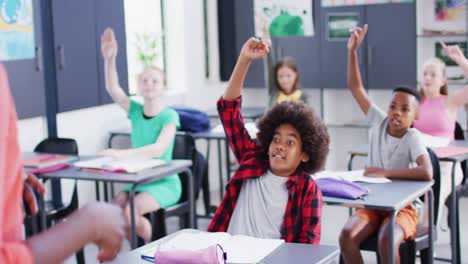 Verschiedene-Lehrerinnen-Und-Glückliche-Schulkinder-An-Schreibtischen,-Die-Im-Klassenzimmer-Die-Hände-Heben