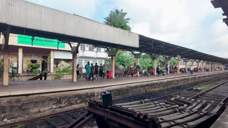 view of kandy railway station in sri lanka, capturing the everyday moments of locals waiting on the platform surrounded by tropical greenery.