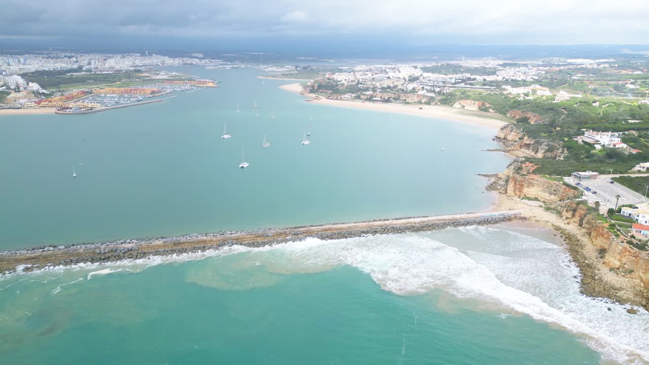 Calm aerial view of Ferragudo coastline, Algarve, with boats and cliffs under clouds