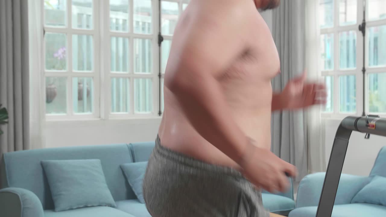 Uomo asiatico robusto senza maglietta che corre su un tapis roulant a casa.