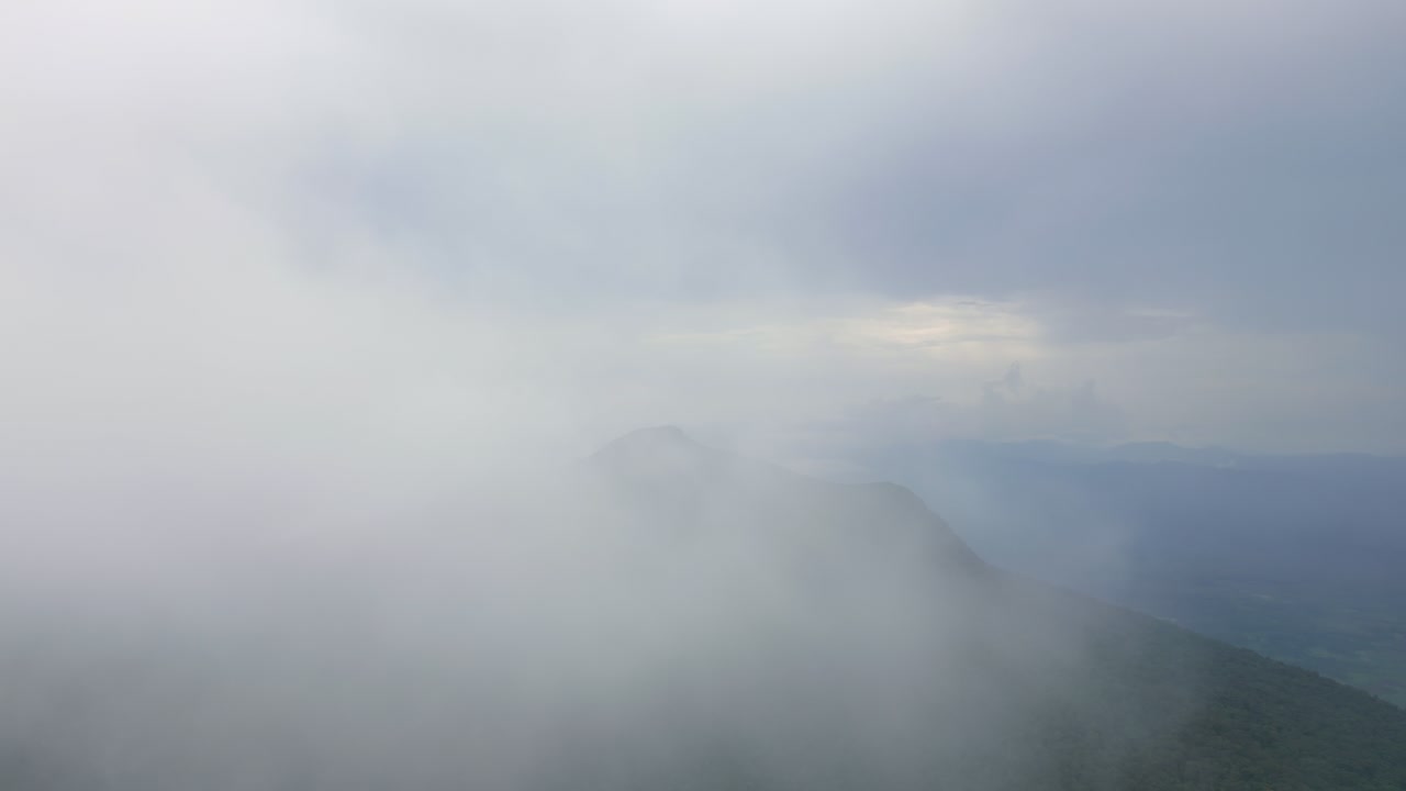 Drone flying through a cloud to reveal a lonely mountain in the distance.