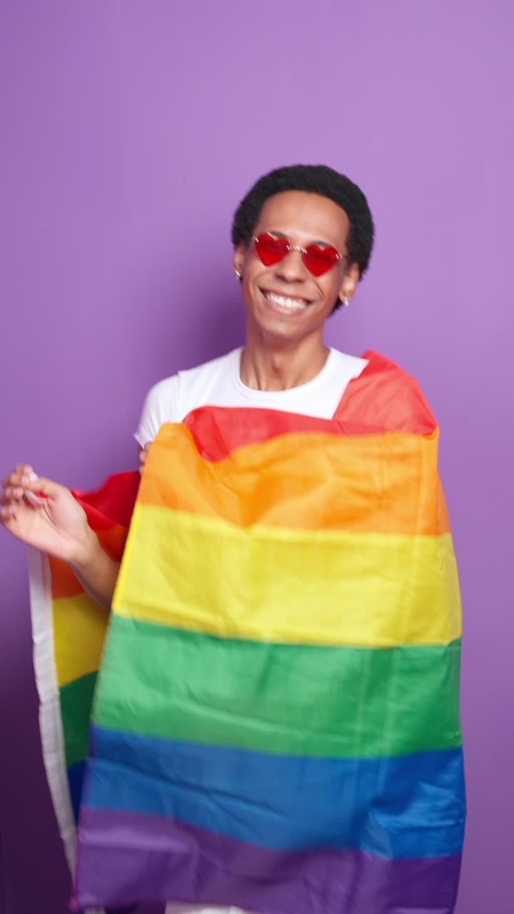 Person with rainbow flag and heart sunglasses celebrating LGBTQ pride