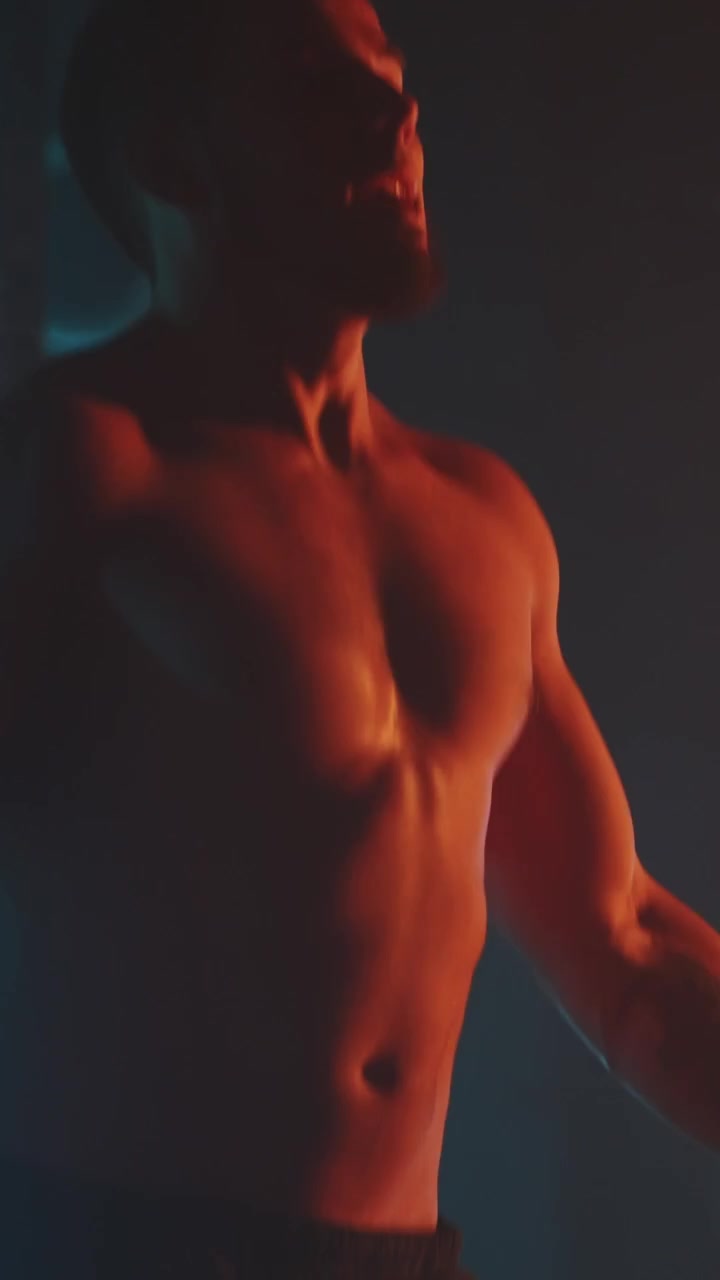 Uomo a torso nudo che salta la corda durante un allenamento intenso in penombra.