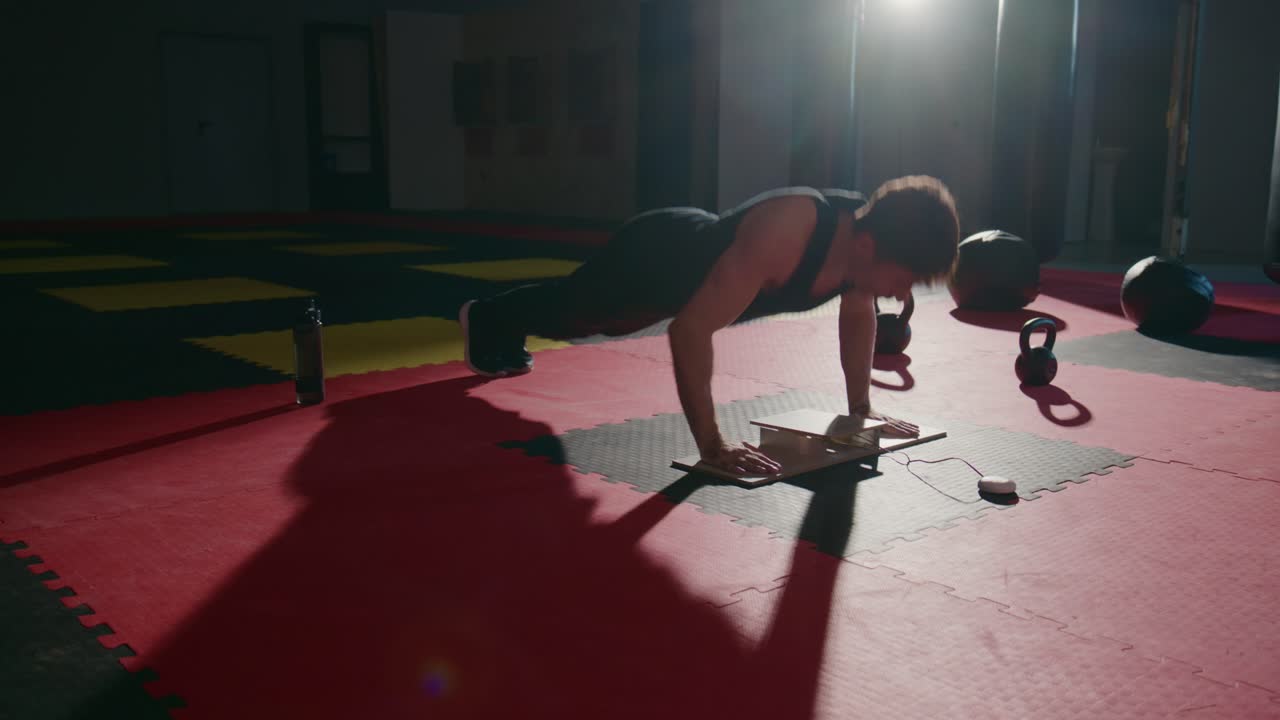 Uomo che fa flessioni su una push-up board in una palestra buia
