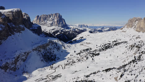 aerial panorama of snow-covered terrain with winding roads at the base of dolomites mountains in italy