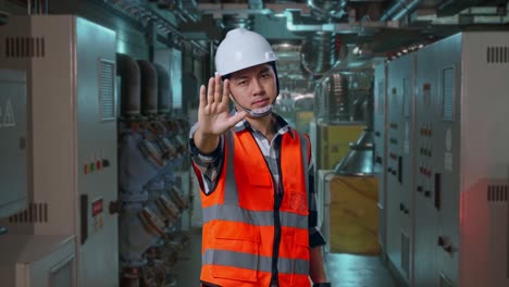 asian male engineer with safety helmet disapproving with no hand sign while standing in engine control room, work of electrical generators
