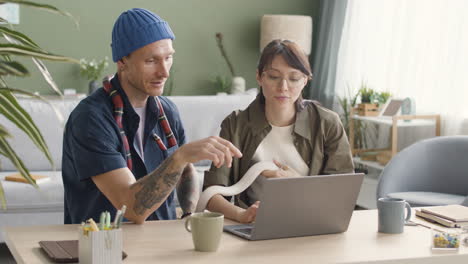 pareja sosteniendo serpientes mascota sentada en el escritorio y usando una computadora portátil