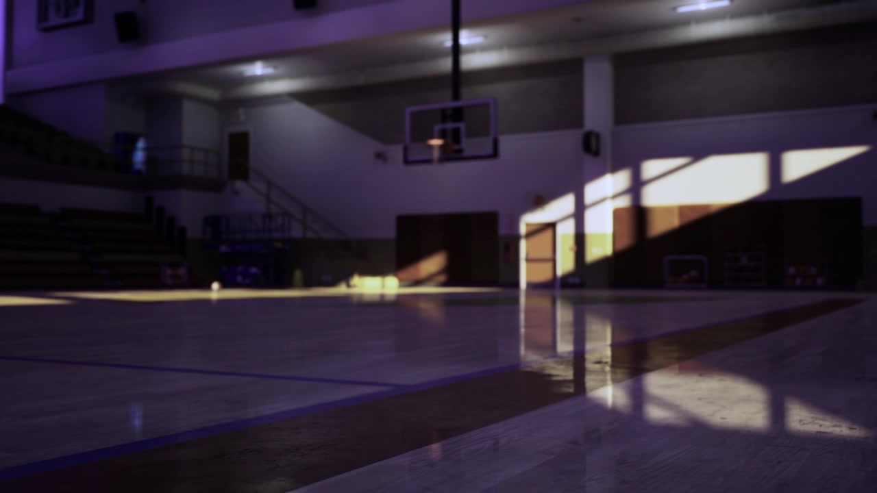 Sunlight shines on smooth gym floor with distant hoop silhouette