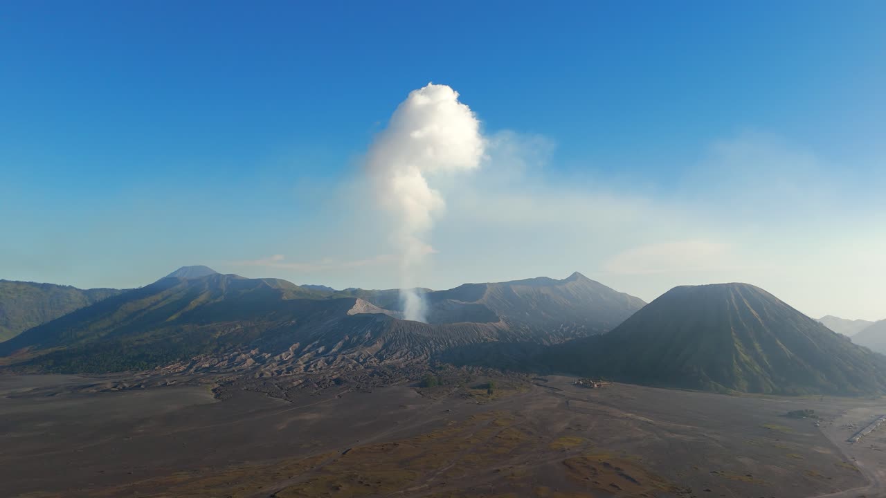Toàn cảnh trên không của núi Bromo và miệng núi lửa Tengger ở Indonesia, với những đỉnh núi lửa, khói trôi và cảnh quan rộng lớn dưới bầu trời xanh trong. Phong cảnh hùng vĩ và không gian trống lớn. Góc máy rộng