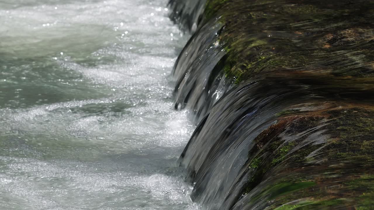 Clear mountain stream flowing over stones covered with green moss and algae