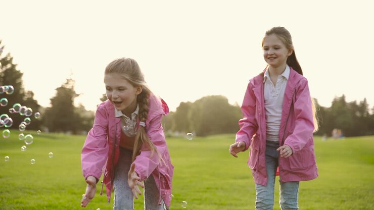 Hermanitas felices con ropa idéntica atrapando burbujas de jabón en el parque 2