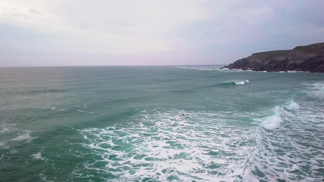surfista nadando a través de olas agitadas junto al promontorio. disparo de dron