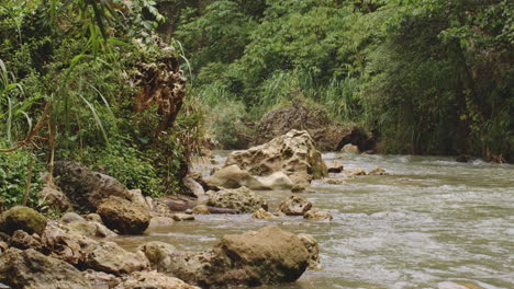 River-Flowing-By-Rock-Formation-Against-Trees-In-Forest-At-Rio-Tanama,-Puerto-Rico---drone-shot